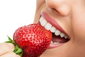 Close-up of a smiling mouth eating a strawberry